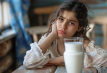 فتاة صغيرة تنظر بتعبير قلق أو متردد إلى كوب من الحليب، مما يجسد فكرة عدم تحمل اللاكتوز