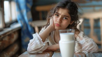 فتاة صغيرة تنظر بتعبير قلق أو متردد إلى كوب من الحليب، مما يجسد فكرة عدم تحمل اللاكتوز