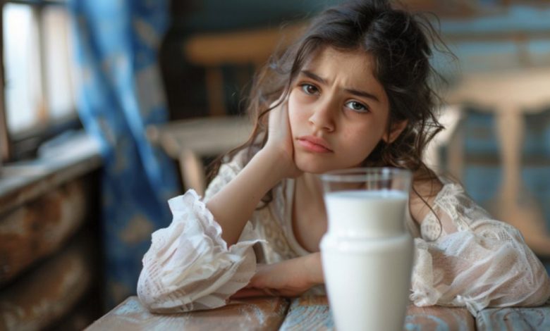 فتاة صغيرة تنظر بتعبير قلق أو متردد إلى كوب من الحليب، مما يجسد فكرة عدم تحمل اللاكتوز