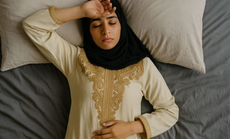 امرأة شابة من أصول شرق أوسطية ترتدي لباسًا تقليديًا مطرزًا وحجابًا أسود، مستلقية على سرير أبيض بنظرة متعبة، ملتقطة من زاوية علوية، تعبر عن الإرهاق العقلي في العصر الحديث